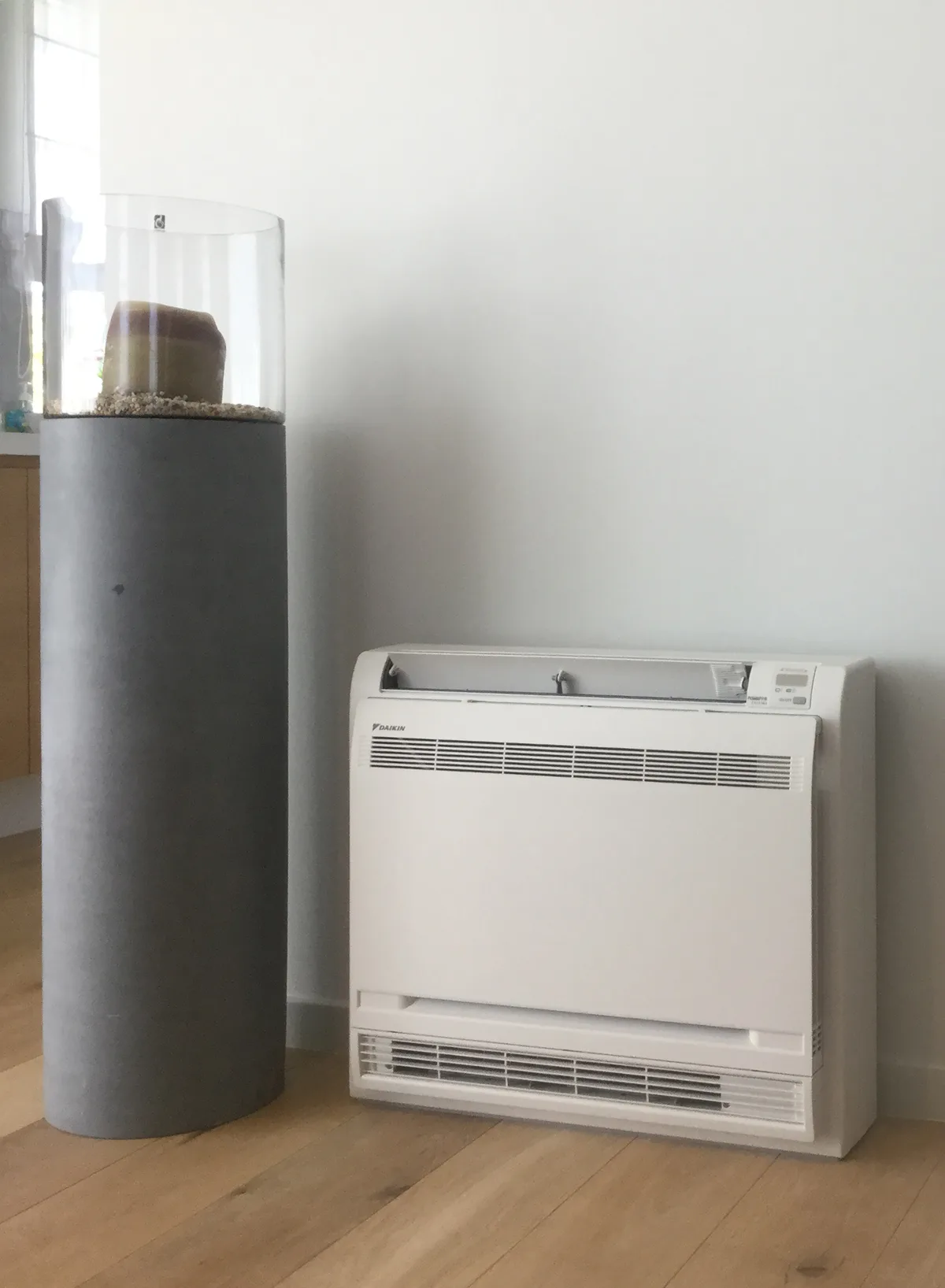Binnenunit in vloermodel tegen de wand van een woonkamer, naast een sokkel op houten vloer
