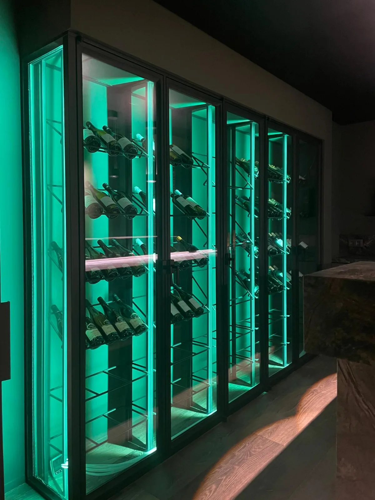 Wijnwand met zwarte glazen deuren en verlichte flessenrekken in een woning